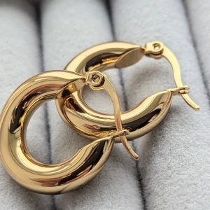 Guldörhängen i rund form - Ett par eleganta örhängen i guld med en rund, tjock form. Örhängena har en slät och blank yta som ger en lyxig känsla. De är designade med en enkel låsmekanism för säker användning.