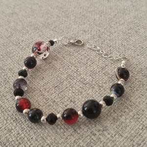 Enkelt armband i svart/rätt - Handgjord armband i svarta och röda pärlor. Små pärlor i svart och glimrar fint. Mått är 17-20 cm, det går att justera utifrån behov.
