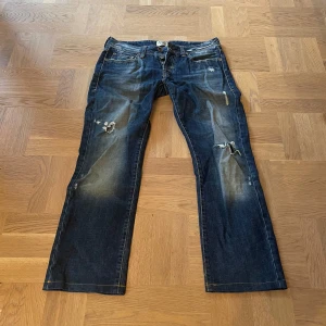 Blå jeansbyxor från Staff - Lågmidjade jeansbyxor från Staff med slitna detaljer/hål och en knappgylf❣️                                   Midjemått= 42 cm                                                           Innerbenslängd= 72 cm