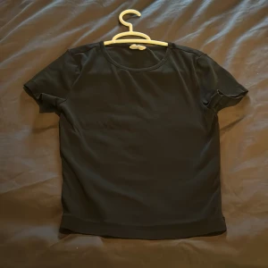Svart kortärmad topp - En enkel och stilren svart kortärmad topp. Toppen har en rund halsringning och är tillverkad i ett mjukt och bekvämt material. Ganska använd som ni ser på lappen men fortfarande i jättebra skick