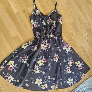 Svart blommig klänning - Hej, säljer denna klänningen, testat den en gång men tyckte inte om den. Den är justerbar vid banden och i mitten, där man kan dra åt beroende på hur man vill att den ska sitta! Perfekt för en sommarkväll 🥰
