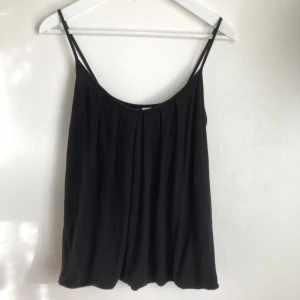 Svart draperat spagetti linne, stl 38, basic, enkelt - Svart spagettilinne, draperad modell, dubbelt tyg med lätt ballongmodell. Tecken på användning finns, något urtvättad och noppor. Mått i cm: bröstvidd 40; axelbandslängd 31; längd fram från axeln 63.