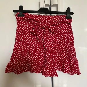 Röd vit blommig rosett knyta bälte kort kjol skort sommarkläder shorts - Stängs med dragkedja i midjan. Har ”shorts” under kjolen.