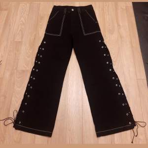 Svarta, vida baggy jeans med öppna sömmar längs benen och vit kontrastsöm. Gothstil. Varken testade eller använda. (Köpt fel storlek). Strlk: M.