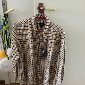 Gant skjorta - Säljer en rutig skjorta från märket ”GANT”, med hänsyn till en allt för liten storlek. Skjortan säljes, som nämnt ovan, i samband med för liten storlek, men även ingen möjlighet till retur. Skjortan är inte använd, sålunda i nyskick.  Köpt för 599kr. Säljes för 150kr. Ifall en önskan av flera bilder önskas är detta en möjlighet.