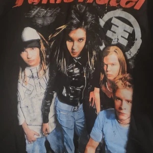 Svart T-shirt med Tokio Hotel-tryck - En svart T-shirt med ett stort tryck av bandet Tokio Hotel på framsidan. T-shirten har korta ärmar och en rund halsringning.
