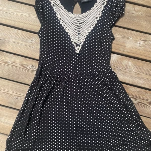 Prickig klänning M - Söt klänning i svart med vita prickar och en spetsdetalj i halsringningen. Klänningen har korta ärmar och en lös passform.  Storlek ca 38/M