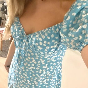 Blommig klänning - Ljusblå blommig klänning från Chiquelle med knytning ifram. Nyskick, aldrig använd.