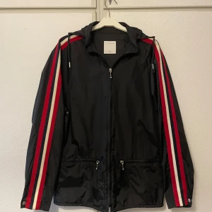 Sandro Regnjacka - Fransk designer - Den är i utmärkt skick och nästan som ny. Storlek S men stor i storlek, passar M. Högkvalitativt material som håller dig torr i alla väderförhållanden. 