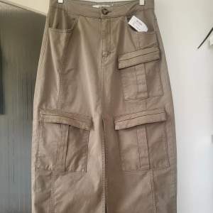 High-waisted cargo skirt in stretchy cotton fabric. The skirt has patch pockets with flaps placed above the knees and one below the hip on the left side. 