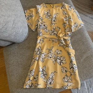 Blommig klänning - Gul fin klänning med vita blommor,, passar till sommar och vår. Har ett midjeband som visa upp figuren om man vill det, har använt 1/2 gånger.