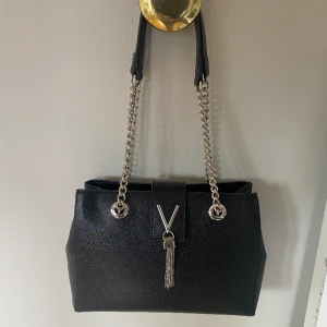 Divana- Valentino Väska - En relativt ny Valentino väska som enbart används fåtal gånger. Väskan är ca 29 cm lång och 23 cm hög, med flertal fack. Väskan stängs med ett magnetlås som är enkelt att stänga. Orginalpris 1 165 kr, pris kan diskuteras.