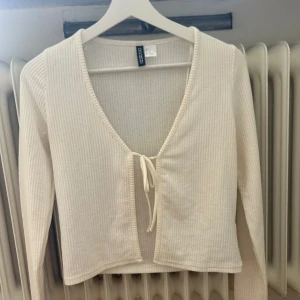 Beige ribbad tröja från Divided - En beige ribbad tröja från hm med långärmad design. Tröjan har en knytning framtill och en v-ringad hals.