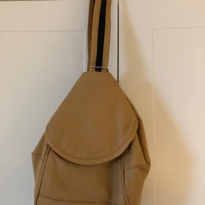 Liten läcker ryggsäck i mjukaste skinn - Kan varieras på olika sätt, se bilder. Många yttre fack och inuti är den fodrad och även där ett fack. Naturfärgat mjukt skinn. 