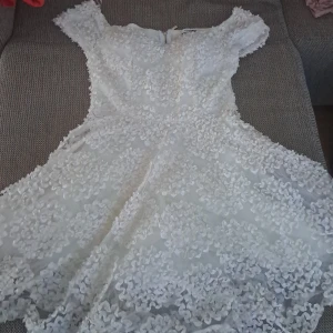 Vit klänning med spetsdetaljer - En vacker vit klänning med spetsdetaljer och blommönster. Klänningen har korta ärmar och en dragkedja på baksidan. Perfekt för festliga tillfällen. jag hade den till studenten 🥰