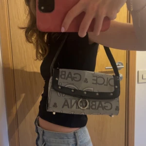 Handväsla - Handväska ”Dolce Gabbana”. Den är köpt second hand för ca 300 kr men tror inte den är äkta🤷 Men tycker det är superfin ändå. Den är lite sliten, kan skicka fler bilder om ni vill ha det.
