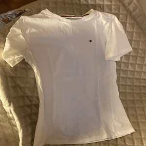 Vit Tommy Hilfiger T-shirt - Vit basic T-shirt från Tommy Hilfiger, använd men i fint skick, inga tydliga defekter  passar xs/s dam