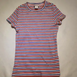En randig t-shirt med färgerna vit, blå, rosa och röda. Den går ganska långt ner på magen, är storlek xxs och är från Monki.