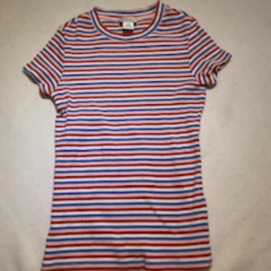 T-shirt  - En randig t-shirt med färgerna vit, blå, rosa och röda. Den går ganska långt ner på magen, är storlek xxs och är från Monki.