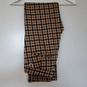 Bruna rutiga byxor - Ett par snygga bruna byxor med rutigt mönster. Tyget är mjukt och bekvämt. De har ganska små fickor på framsidan och fickorna på baksidan är fake. Nypris: 599 kr