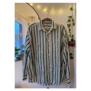Randig skjorta  - Säljer denna supersnygga skjorta från F.O.B Cargo i stl L. Kan bäras i oversize-modell för S-M också. Vit med mörkgröna och gråa ränder. Köpt på second hand och i fint skick✨ skriv om du har frågor :) 