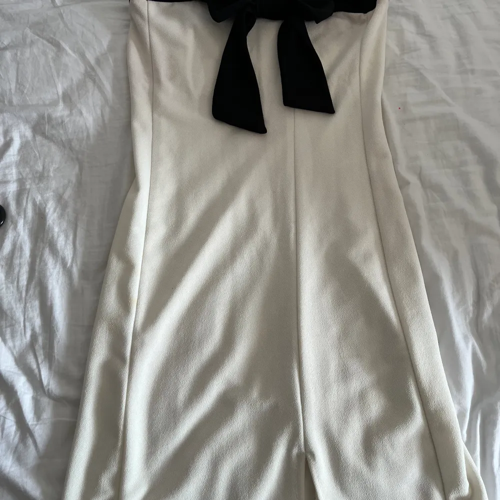 En vit off shoulder miniklänning med en svart rosett uppepå. I väldigt bra skick använd Ksk 2 ggr. Vet inte vilken storlek men passar mig perfekt o jag är strl S.. Klänningar.
