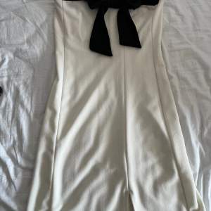 En vit off shoulder miniklänning med en svart rosett uppepå. I väldigt bra skick använd Ksk 2 ggr. Vet inte vilken storlek men passar mig perfekt o jag är strl S.