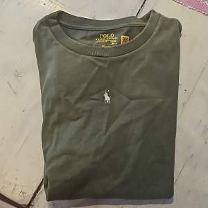 Grön t-shirt från Polo Ralph Lauren med en broderad vit logotyp på bröstet. T-shirten har korta ärmar och en rund halsringning.