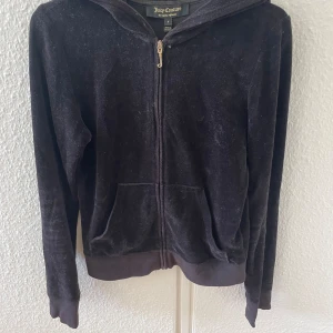 Svart velourjacka från Juicy Couture - En svart velourjacka från Juicy Couture med dragkedja framtill och huva. Jackan har ett stort Juicy Couture-tryck på ryggen i leopardmönster med rosa detaljer.