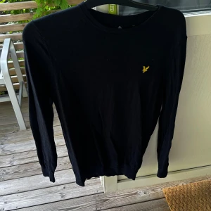 Svart långärmad tröja med gul logotyp - En svart långärmad tröja med en gul logotyp på bröstet. Tröjan har en rund hals och är tillverkad i ett mjukt material.