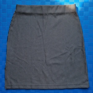 Grå kjol från Joelle - En elegant grå kjol från Joelle med vita ränder. Kjolen är tillverkad av 100% polyester och har en liten slits på sidan.