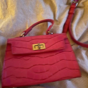 Rosa Väska, axelband  - Säljer denna fina rosa väska från Glitter! Hårt material med silver och guld detaljer!  Den har en ficka med dragkedja inuti😍 dessutom finns tillhörande axelband!  perfekt till att piffa upp en outfit😍  Den är bara använd 2 gånger, så den är som ny!