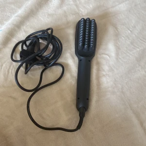 Svart elektrisk hårborste från Miss - En svart elektrisk hårborste från Miss med en digital display och två knappar för att justera temperaturen. Borsten har en sladd för strömförsörjning och är designad för att enkelt kunna reda ut och styla håret.