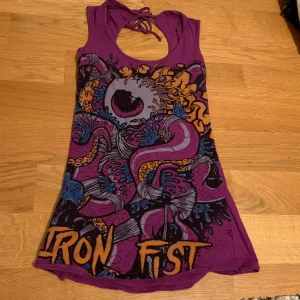 Lila iron fist linne - Långt Urringat lila linne med tryck, är även öppen i ryggen.