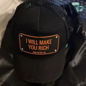 I Will make you rich Keps - Feta keps från JOHN&CO HATTER  De är svart färgat och orange på texter. Kan prata om priset 