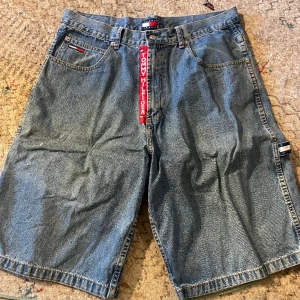 Vintage Tommy Hilfiger Jeansshorts - Riktigt fina Hilfiger jeansshorts, troligen från 2000-talets början eller sent 90-tal. Passar bäst för längre personer över 175 cm, men fungerar för alla över 160 cm som gillar lösa kläder. Två små hål syns på framsidan pga en skateolycka, storlek 36