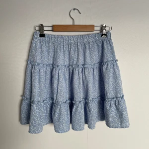 Blå volangkjol - Aldrig använd. Fint växtligt mönster. Resår i midjan. Storlek S men är mer som en M. DM för fler bilder.