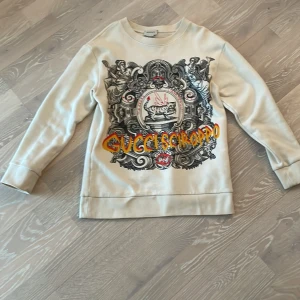En exklusiv limited edition Gucci tröja perfekt för våren - 41 cm i midjan.  40 cm i ärmen. 57 cm i längd Strlek 10 år i barn Färg: biege material: 100% bomull  Nypris: 2500kr
