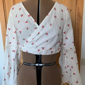 Omlott-topp - Sååå fin omlott-topp med körsbär och trumpetärmar! 100% bomull, aldrig använd. Märkt storlek M, men eftersom det är omlott är den justerbar till S-M.