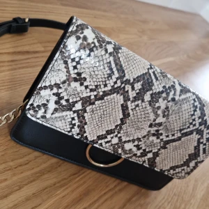 Handväsk med snake print  - Axelremsväska med snake print och gulddetaljer. Finns en lite ficka och korthållare på insidan av väskan. Sparsamt använd.