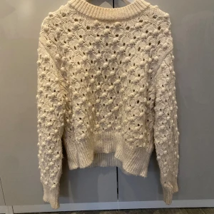 Stickad tröja med detaljer på  - Skön tröja i en créme vit färg. Säljer pga att den inte kom till användning. Tveka inte att höra av dig för mer bilder.