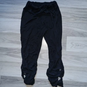 Svarta byxor med dekorativa detaljer - Svarta leggings med elastisk midja och dekorativa detaljer vid bensluten. Byxorna har en lös passform och är dekorerade med pärlor och blingbling. stl 146/152