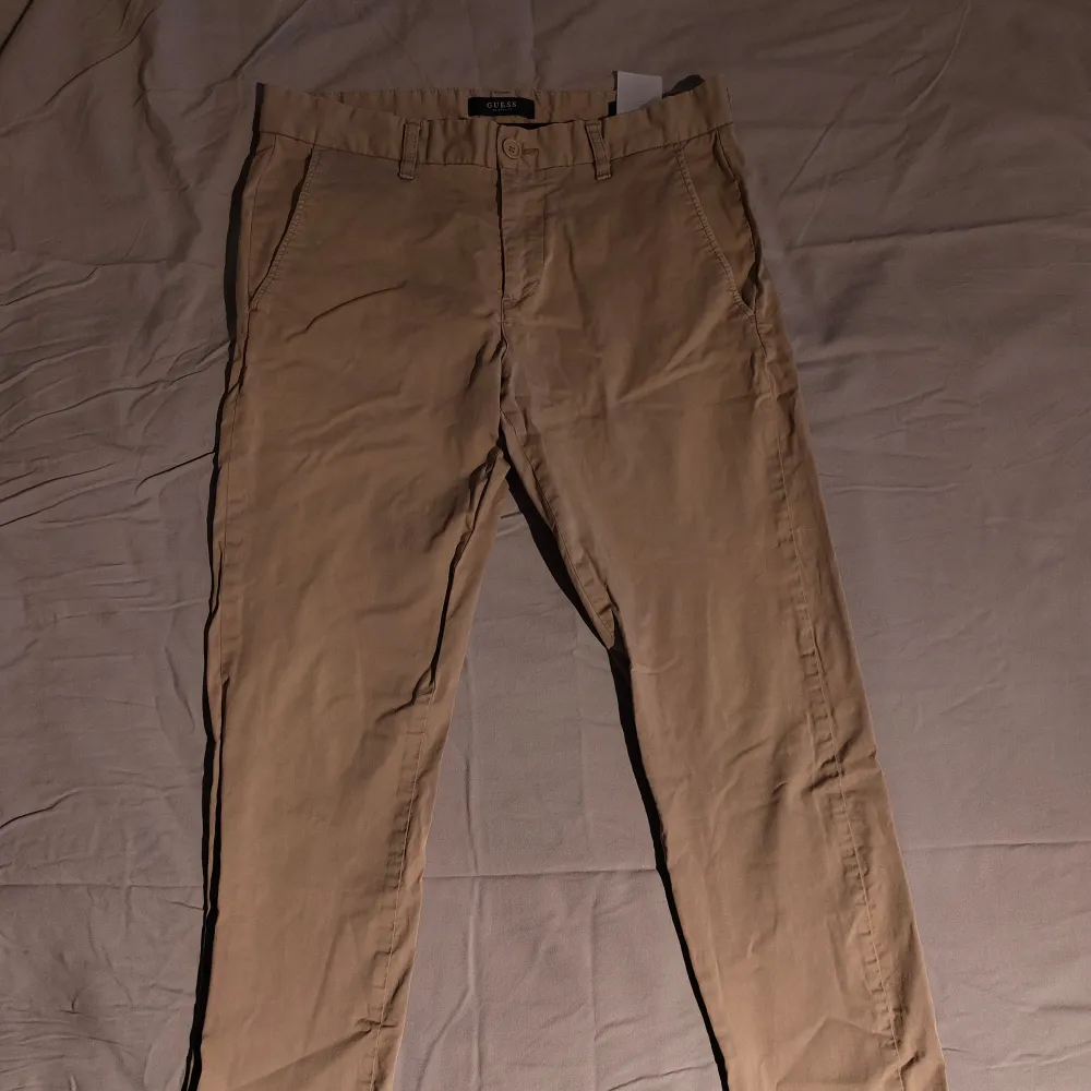 Ett par beige byxor från Guess i storlek W31 L31/32. Byxorna har en klassisk design med knapp och dragkedja framtill samt hällor för bälte.. Jeans & Byxor.