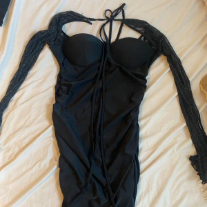 Svart klänning  - Svart klänning med shimmer detalj på ärmarna med en knytning runt halsen.