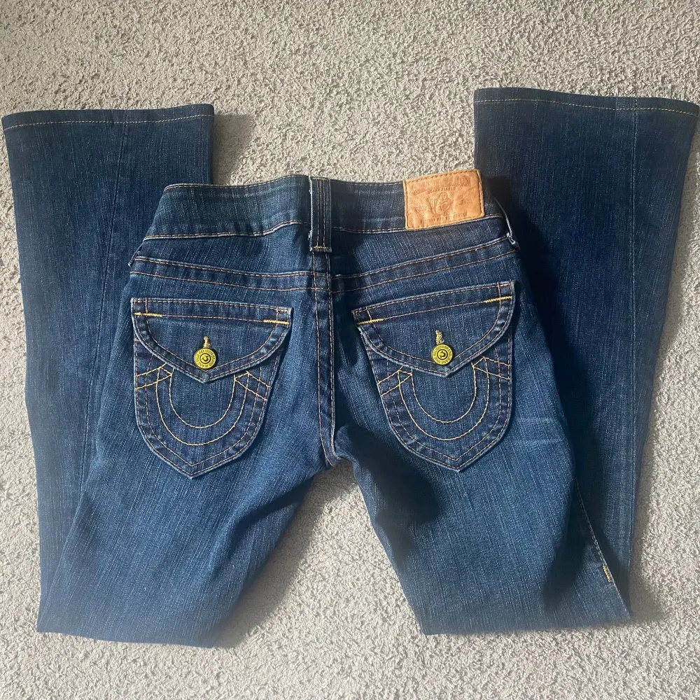 Säljer dessa fina mörkblå truereligion jeans med gula detaljer! De är i mycket bra skick och är lågmidjade bootcut!! Midjemåttet är 37cm och innerbenslängden är 72 cm💗Storleken är runt XXS-XS!!. Jeans & Byxor.