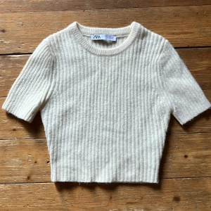 Beige ribbad tröja från Zara - En stilren och bekväm vit ribbad tröja från Zara. Tröjan har korta ärmar och en rund halsringning, kort modell. Perfekt för både vardag och fest. Skicka dm vid frågor.