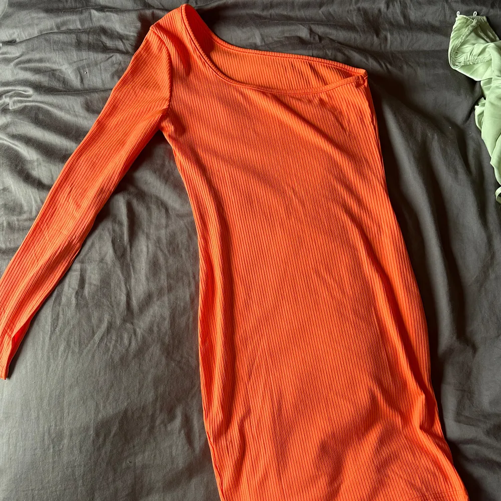 En orange ribbad klänning med långärmad design. Klänningen har en tight passform och är tillverkad i ett bekvämt material. Perfekt till neon fest. Klänningar.