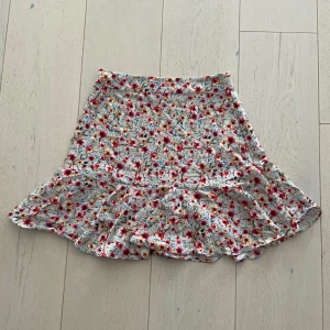 Blommig kort kjol - Jättefin sommarkjol som tyvärr har blivit för liten i midjan för mig. Endast använd ett fåtal gånger, fint skick, silkigt material (polyester), kort modell med diskret dragkedja på sidan.🙌🏻🌸