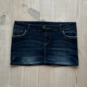 Lågmidjad jeanskjol  - Lågmidjad jeanskjol från Yessica som jag har sytt upp från en längre kjol. Kan inte hitta storlek men skulle säga S/M. Tvärs över midjan är det 39 cm + stretch och längs med sidan är det 28 cm. Fint skick. Använd gärna köp nu!