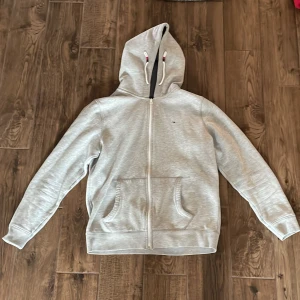  Grå Tommy hilfigare zip up hoddie - Snygg Tommy hilfigare hoddie i kollektion med Tommy jeans perfekt nu till våren och sommaren. Nypris 1300kr    Storlek L men fungerar också som M 